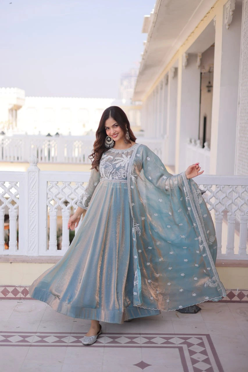 Woman in a light blue traditional outfit standing on a balcony with a white building in the background.